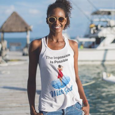 Lightweight Bella+Canvas tank top made from preshrunk cotton with “Impossible Woman” design message, “The Impossible Is Possible with God,” inspirational apparel encouraging women to walk in step with God who makes our impossible dreams become real, woman at the beach wearing white tank top